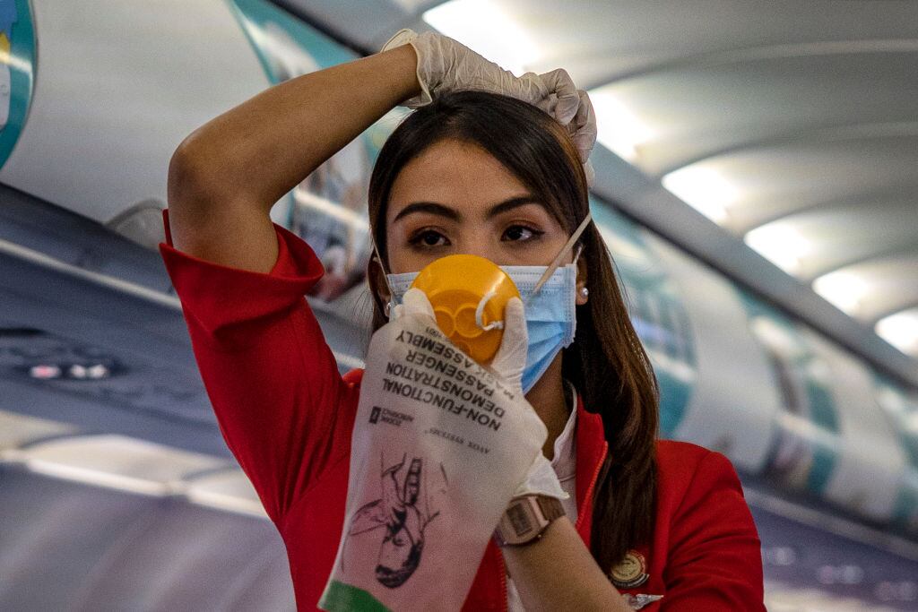 Una asistente de vuelo enseña medidas de protección utilizando una mascarilla por el coronavirus