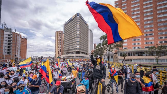 BOGOTA, COLOMBIA - MAY 05: A demonstrator waves a Colombian flag while others walk by as part of a march during national strike on May 5, 2021 in Bogota, Colombia. Despite that the ruling party announced withdrawal of the unpopular bill for a tax reform and the resignation of the Minister of Finances, social unrest continues after a week. The United Nations human rights office (OHCHR) showed its concern and condemned the riot police repression. Ongoing protests take place in major cities since April 28. (Photo by Diego Cuevas/Getty Images)