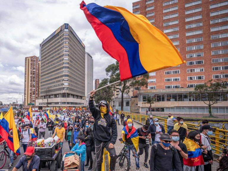 BOGOTA, COLOMBIA - MAY 05: A demonstrator waves a Colombian flag while others walk by as part of a march during national strike on May 5, 2021 in Bogota, Colombia. Despite that the ruling party announced withdrawal of the unpopular bill for a tax reform and the resignation of the Minister of Finances, social unrest continues after a week. The United Nations human rights office (OHCHR) showed its concern and condemned the riot police repression. Ongoing protests take place in major cities since April 28. (Photo by Diego Cuevas/Getty Images)