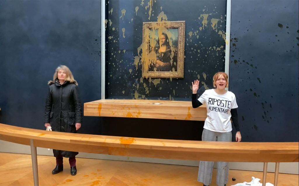This image grab taken from AFPTV footage shows two environmental activists from the collective dubbed "Riposte Alimentaire" (Food Retaliation) gesturing as they stand in front of Leonardo Da Vinci's "Mona Lisa" (La Joconde) painting after hurling soup at the artwork, at the Louvre museum in Paris, on January 28, 2024. Two protesters on January 38, 2024 hurled soup at the bullet-proof glass protecting Leonardo da Vinci's "Mona Lisa" in Paris, demanding the right to "healthy and sustainable food", an AFP journalist said. It is the latest attack on the masterpiece in the French capital's Louvre museum, after someone threw a custard pie at it in May 2022, but it's thick glass casing ensured it came to no harm. (Photo by David CANTINIAUX / AFPTV / AFP) (Photo by DAVID CANTINIAUX/AFPTV/AFP via Getty Images)