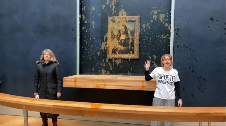 This image grab taken from AFPTV footage shows two environmental activists from the collective dubbed "Riposte Alimentaire" (Food Retaliation) gesturing as they stand in front of Leonardo Da Vinci's "Mona Lisa" (La Joconde) painting after hurling soup at the artwork, at the Louvre museum in Paris, on January 28, 2024. Two protesters on January 38, 2024 hurled soup at the bullet-proof glass protecting Leonardo da Vinci's "Mona Lisa" in Paris, demanding the right to "healthy and sustainable food", an AFP journalist said. It is the latest attack on the masterpiece in the French capital's Louvre museum, after someone threw a custard pie at it in May 2022, but it's thick glass casing ensured it came to no harm. (Photo by David CANTINIAUX / AFPTV / AFP) (Photo by DAVID CANTINIAUX/AFPTV/AFP via Getty Images)