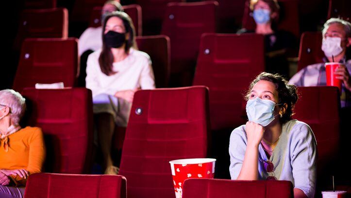 Audience at the cinema wearing protective face masks and sitting on a distance while watching the movie.