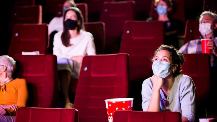 Audience at the cinema wearing protective face masks and sitting on a distance while watching the movie.