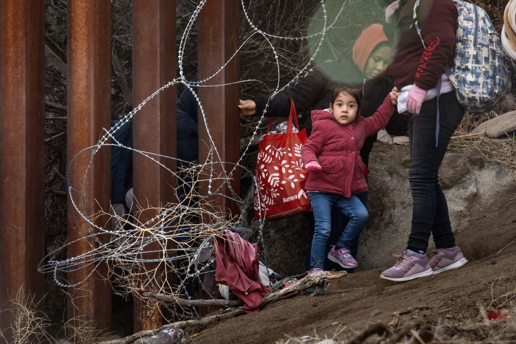 Una familia migrante con una niña pequeña cruzan la frontera desde México hacia el Estado de California en Estados Unidos