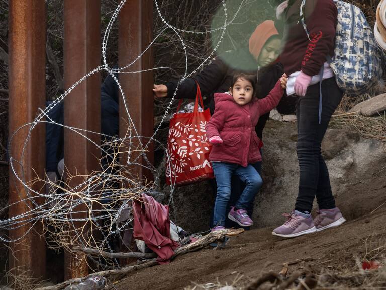 Una familia migrante con una niña pequeña cruzan la frontera desde México hacia el Estado de California en Estados Unidos