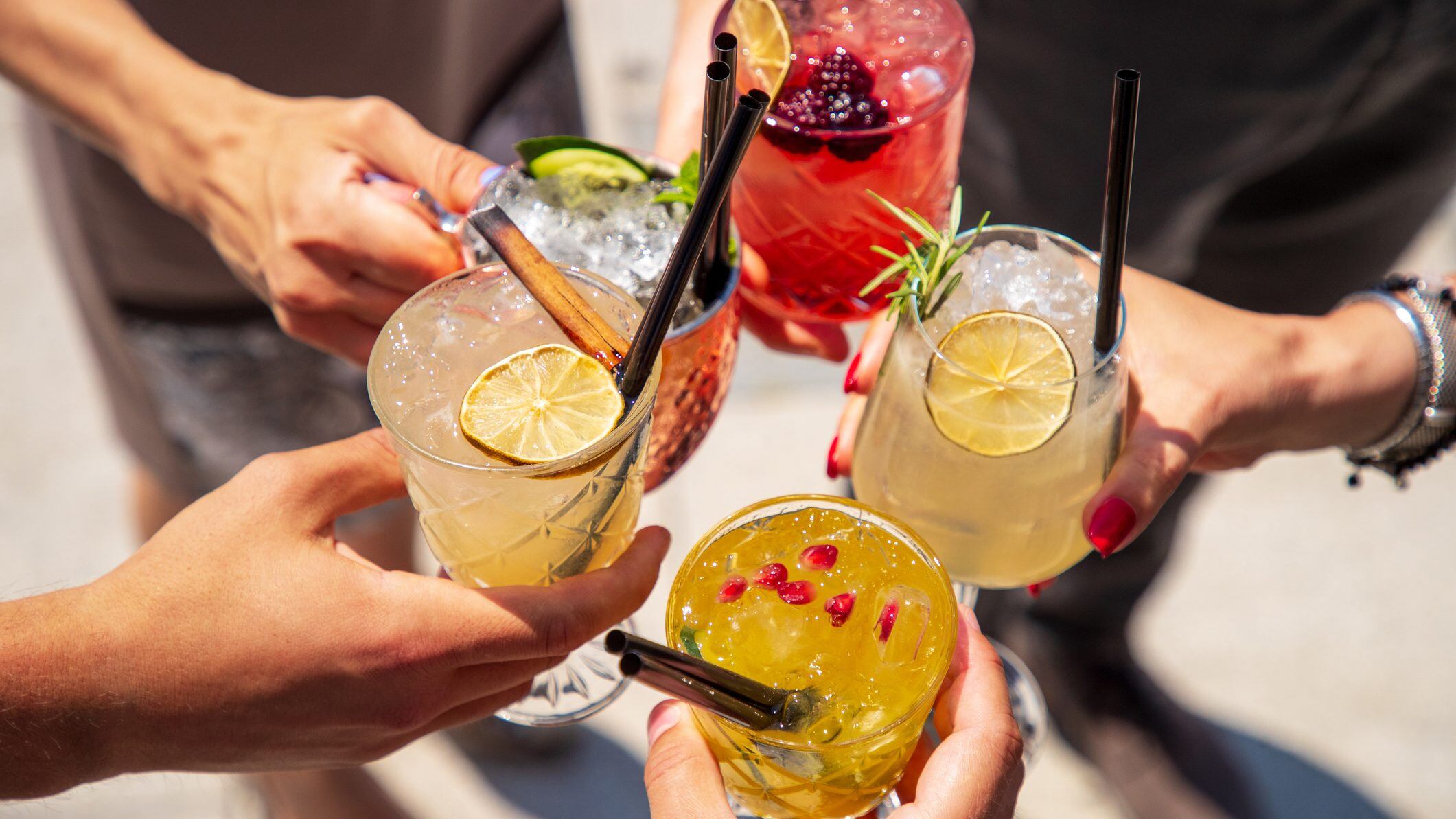 Five exotic cocktails on ice in hands joined in celebratory toast