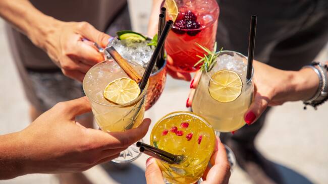 Five exotic cocktails on ice in hands joined in celebratory toast