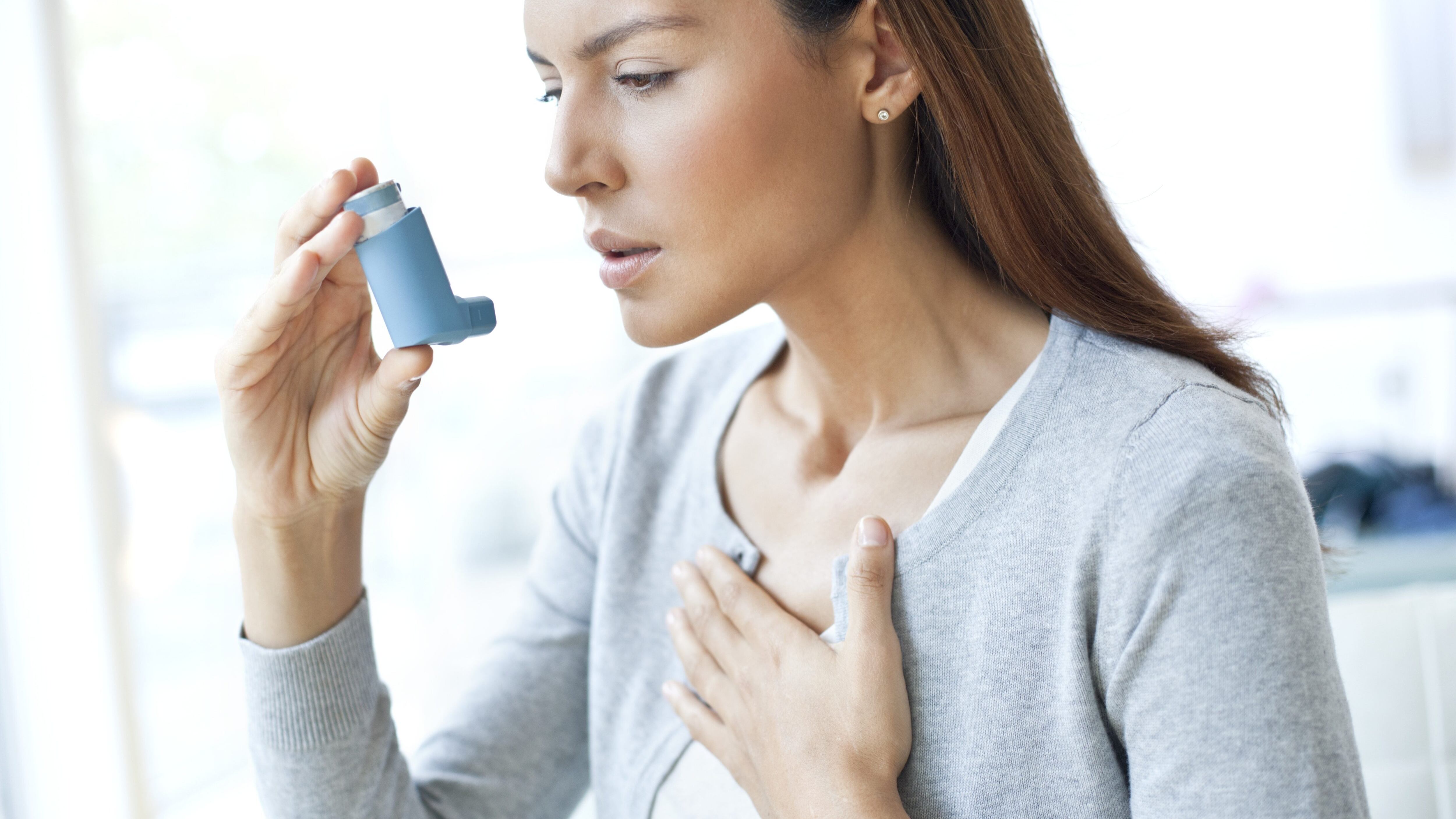 MODEL RELEASED. Young woman using an inhaler and touching her chest.