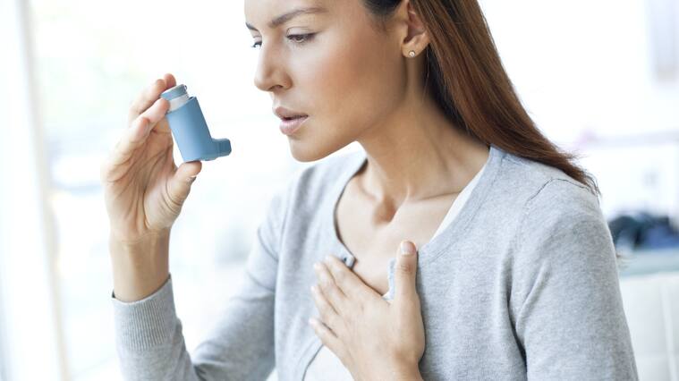 MODEL RELEASED. Young woman using an inhaler and touching her chest.