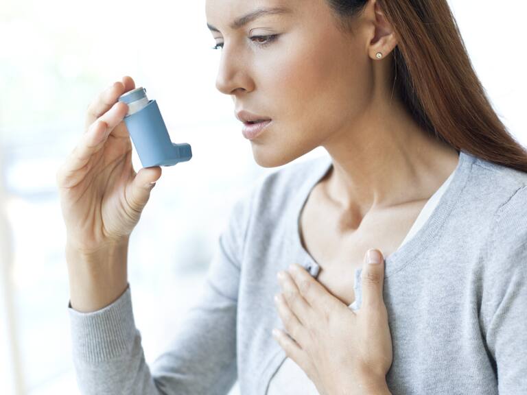 MODEL RELEASED. Young woman using an inhaler and touching her chest.