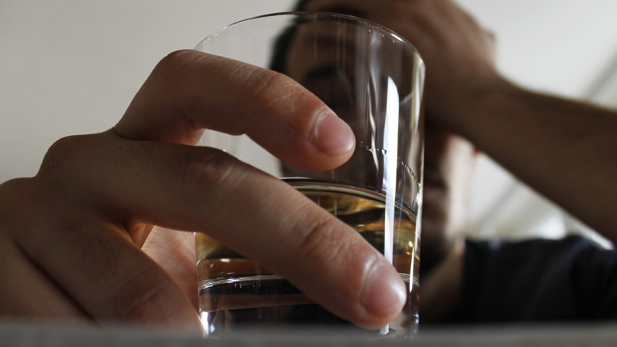 Drunk young adult male holding glass of alcohol, studio shot.