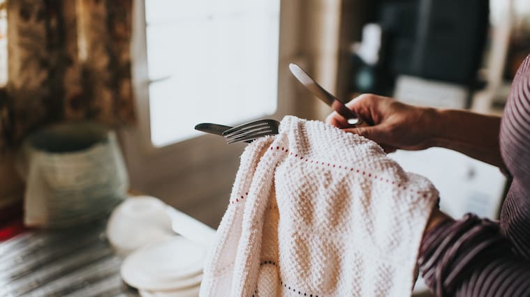 Woman in a kitchen with dish cloth, drying cutlery.
