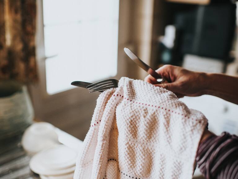 Woman in a kitchen with dish cloth, drying cutlery.