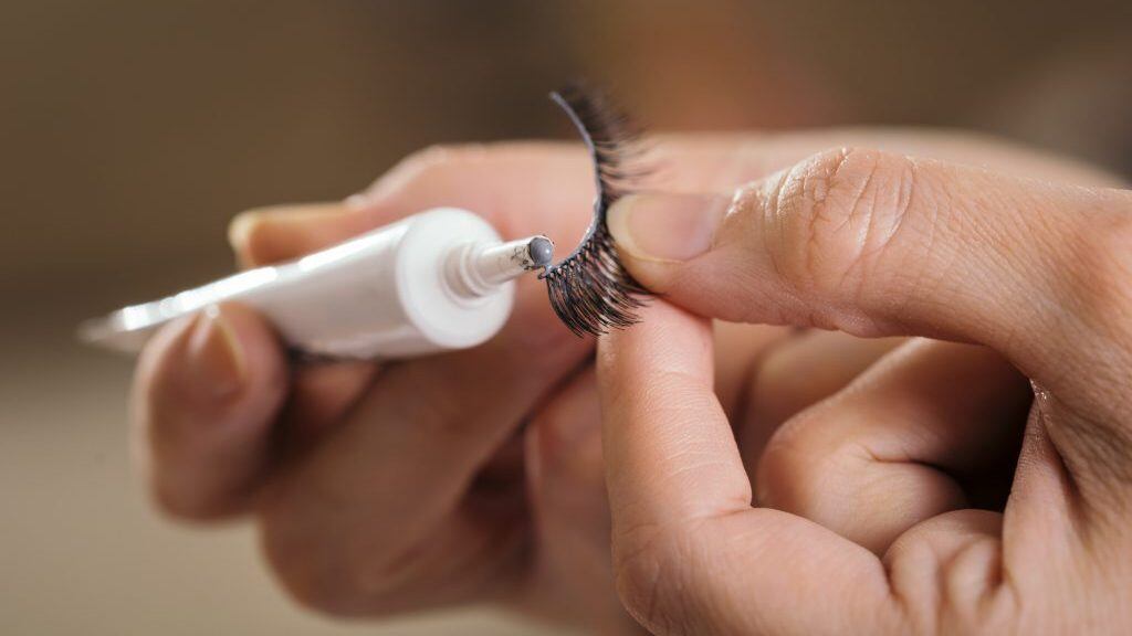 Detail of make up artist's hands adding glue on artificial eyelashes while doing a client's make up