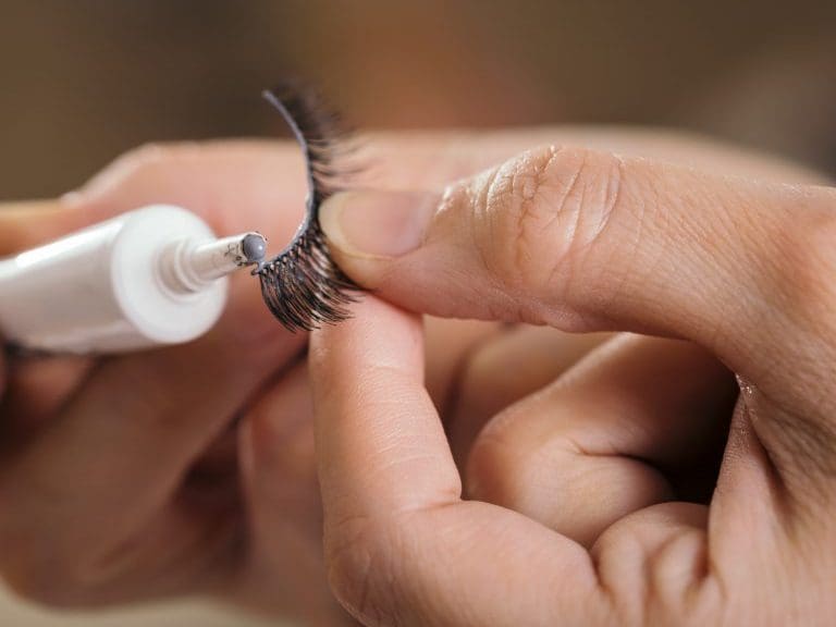 Detail of make up artist's hands adding glue on artificial eyelashes while doing a client's make up