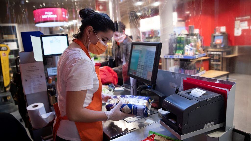 An cashier wearing a protect mask and gloves stand behind plastic sheeting at a checkout, at a Franprix supermarket in Paris, on April 8, 2020, on the twenty third day of a strict lockdown in France aimed at curbing the spread of the COVID-19 pandemic, caused by the novel coronavirus. (Photo by Thomas SAMSON / AFP) (Photo by THOMAS SAMSON/AFP via Getty Images)