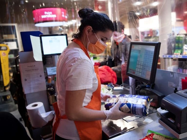 An cashier wearing a protect mask and gloves stand behind plastic sheeting at a checkout, at a Franprix supermarket in Paris, on April 8, 2020, on the twenty third day of a strict lockdown in France aimed at curbing the spread of the COVID-19 pandemic, caused by the novel coronavirus. (Photo by Thomas SAMSON / AFP) (Photo by THOMAS SAMSON/AFP via Getty Images)