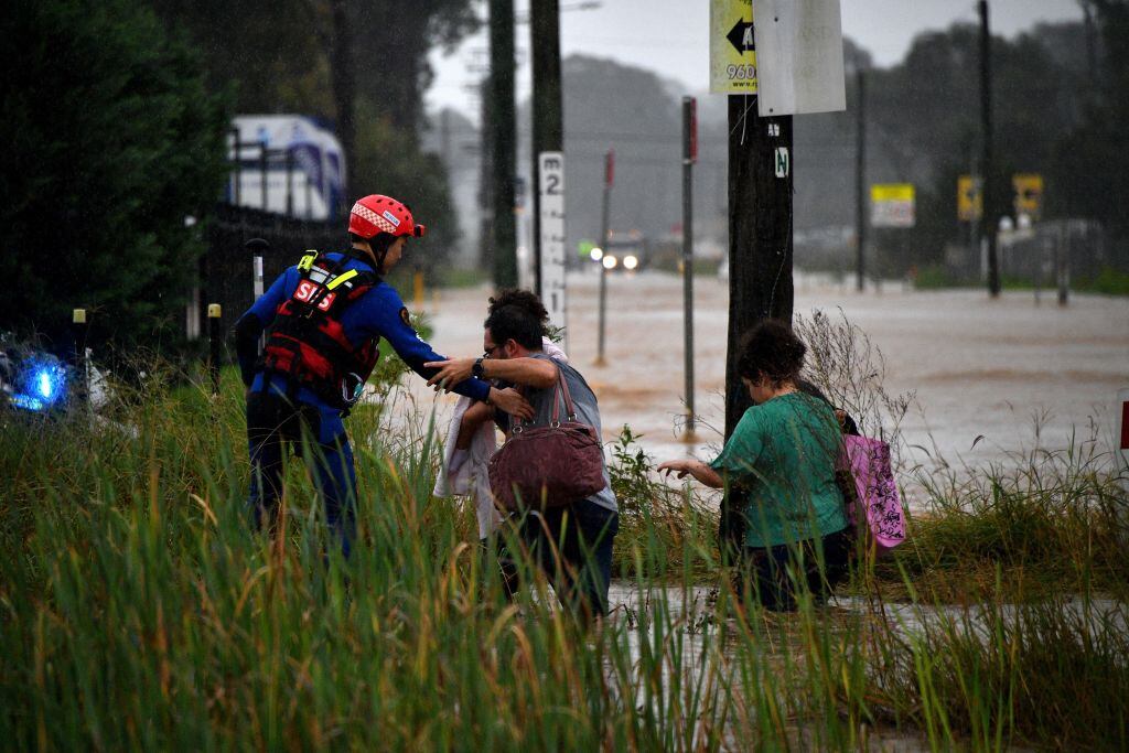 Rescatista ayuda dos personas a salir de una calle inundada en Sidney