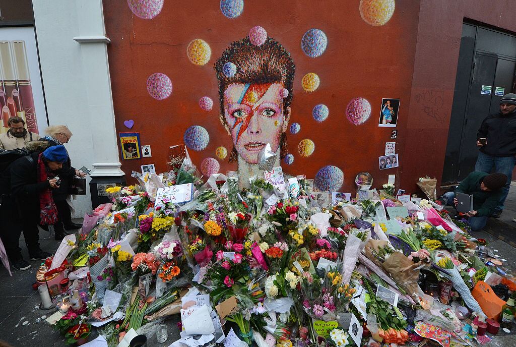 LONDON, ENGLAND - JANUARY 12: Fans and wellwishers gather to pay tribute to David Bowie at a mural in South London, on January 12, 2016 in London, England. British music and fashion icon David Bowie died yesterday at the age of 69 following an 18 month battle with cancer. The 'Aladdin Sane' mural has become something of an unofficial focal point for grieving fans as it is situated in his hometown of Brixton. (Photo by Jim Dyson/Getty Images)