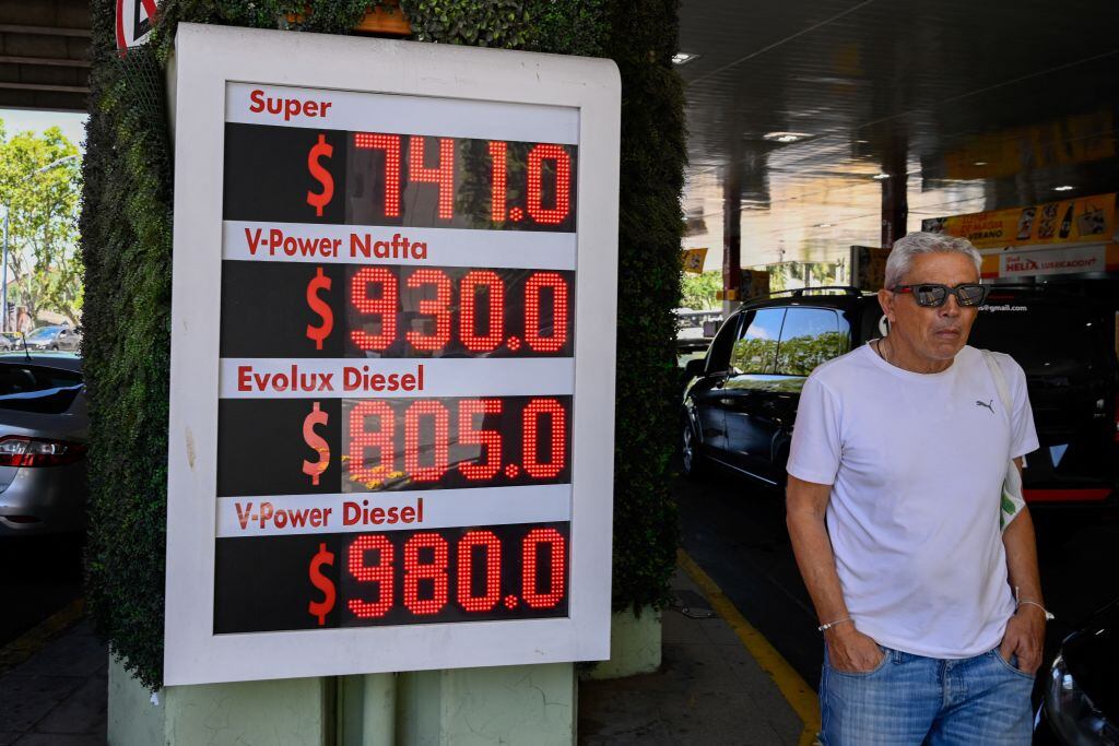Un hombre camina por una estación ante el cartel que muestra el fuerte aumento en el precio de los combustibles en Argentina durante el gobierno de Milei.