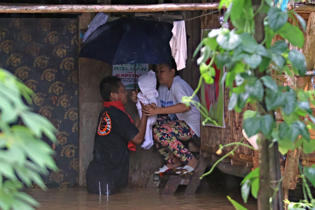 Pareja saca a su bebé ante la inundación que afecta a su hogar tras el paso de la tormenta tropical Jelawat en la isla de Mindanao en Filipinas.