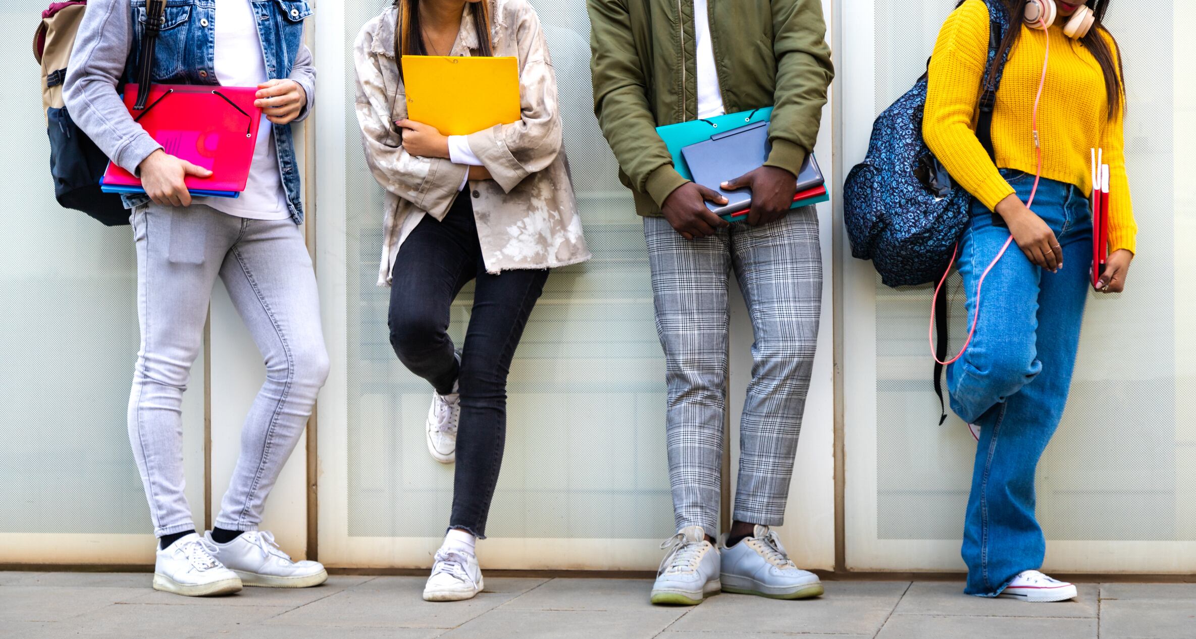 Group of multiracial teenage college students ready to go back to school standing against blue background wall. Higher education concept.