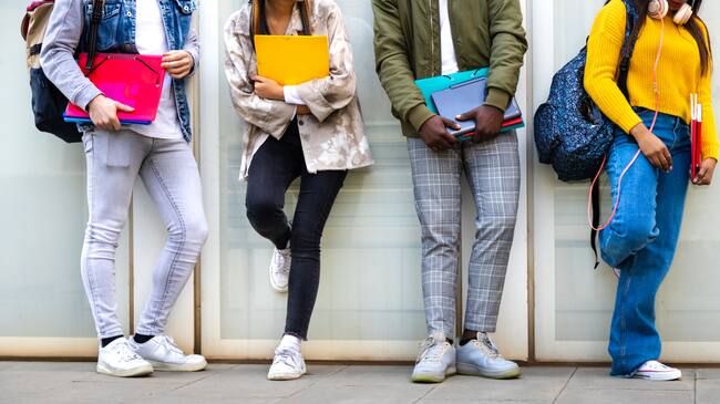 Group of multiracial teenage college students ready to go back to school standing against blue background wall. Higher education concept.