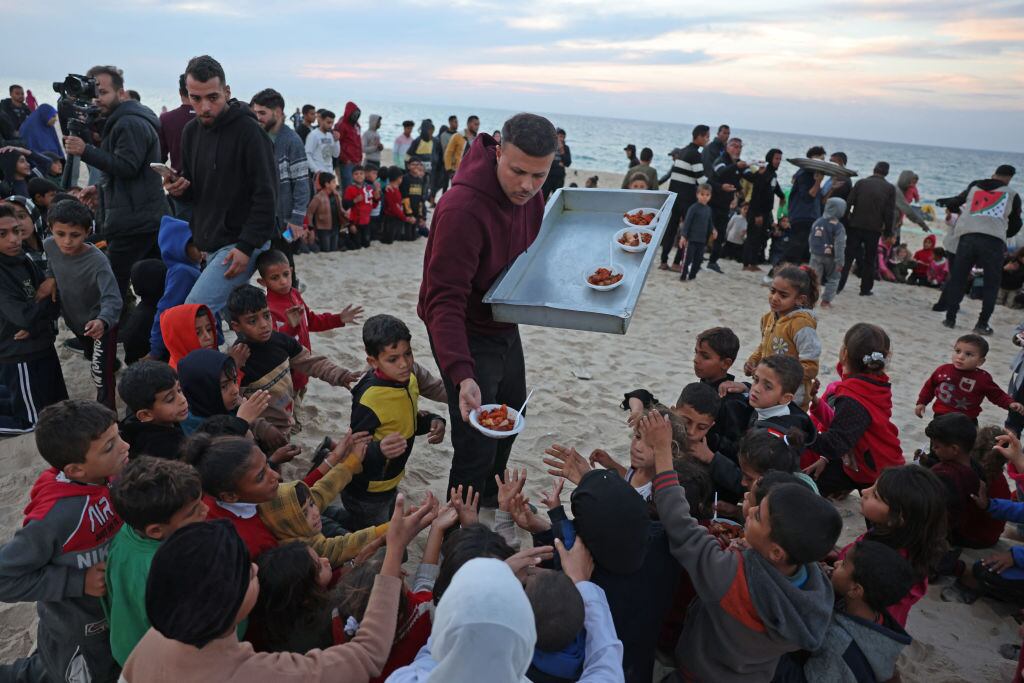 Un cocinero palestino entrega alimentos a un grupo de niños cerca del mar Mediterráneo en la Franja de Gaza