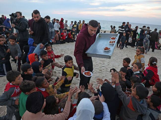 Un cocinero palestino entrega alimentos a un grupo de niños cerca del mar Mediterráneo en la Franja de Gaza