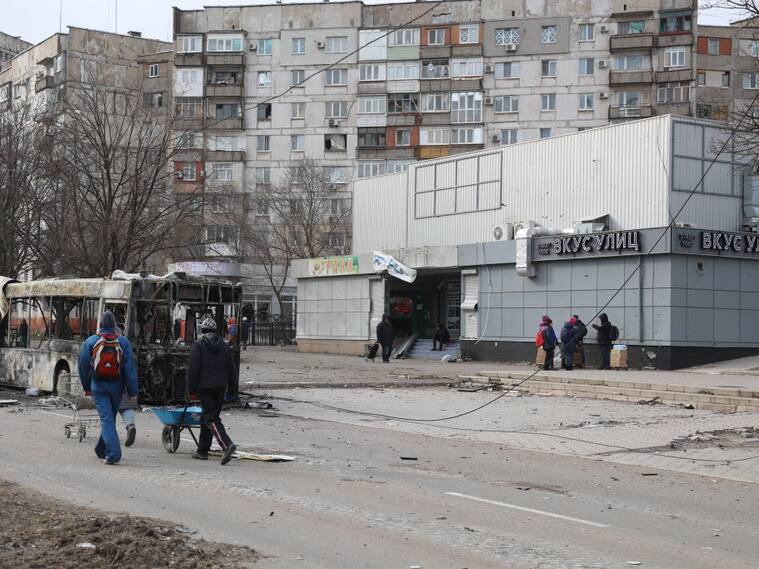 Personas caminan frente a un edificio dañado por los ataques en Mariúpol