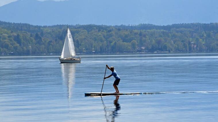 dpatop - 19 April 2020, Bavaria, Tutzing: A sailboat and a stand-up paddler drift on the unusually empty Starnberger See. Due to the exit restrictions of the Corona - Pandemic, no excursionists can reach the otherwise besieged lake despite early summer temperatures and sunshine. Photo: Ursula Düren/dpa (Photo by Ursula Düren/picture alliance via Getty Images)