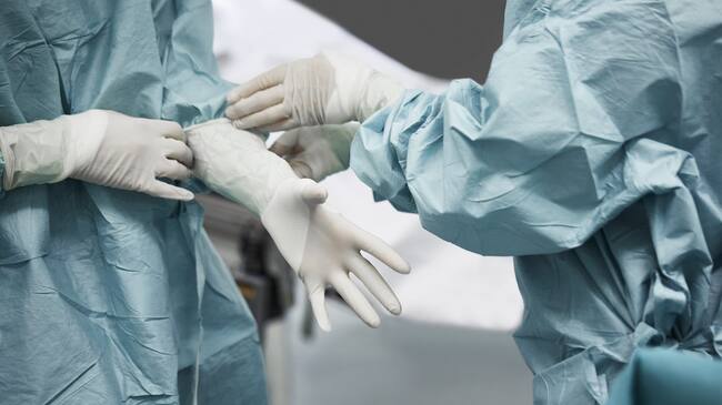 Midsection of female doctor helping surgeon wearing surgical glove. Medical colleagues are preparing for surgery. They are standing in emergency room.