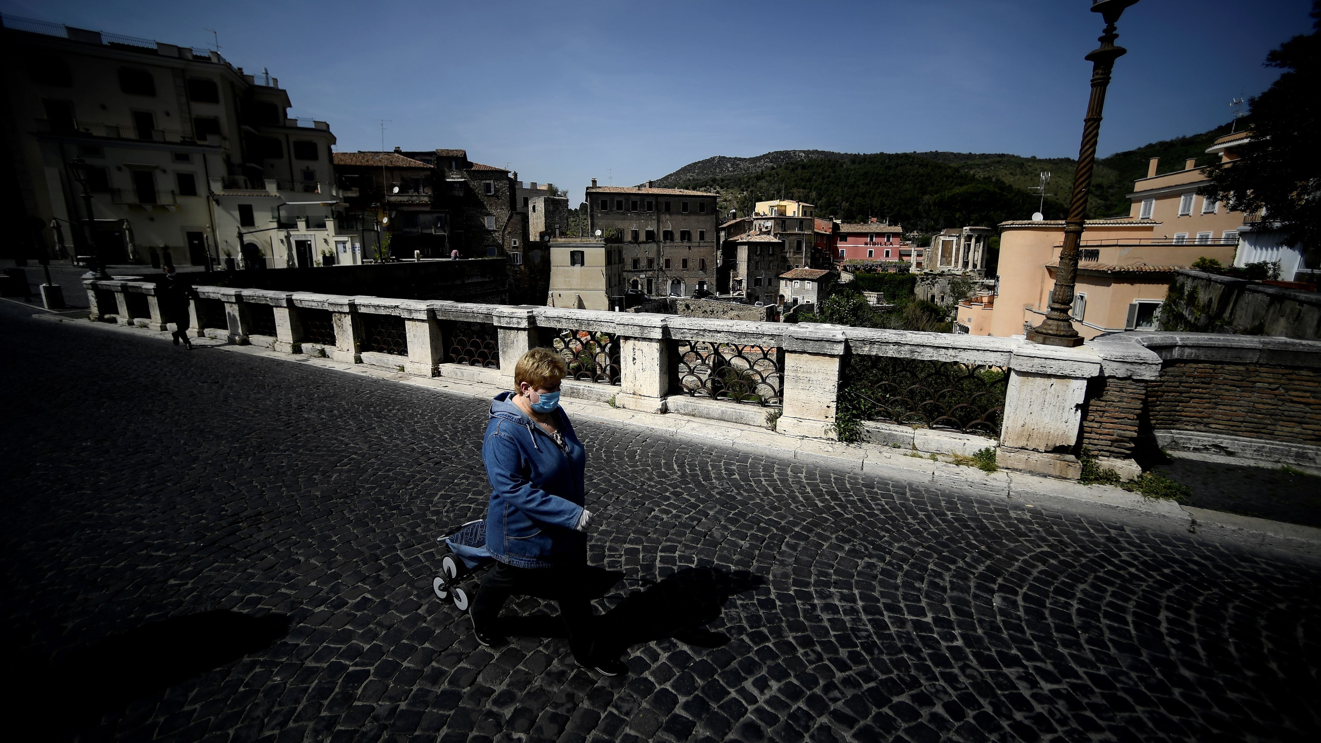 A woman wearing a face mask   walks on an empty Gregoriano bridge in central Tivoli on April 17, 2020, during a lockdown aimed at curbing the spread of the COVID-19 pandemic, caused by the novel coronavirus. - The coronavirus lockdown is putting tourist towns across Italy at risk, such as Tivoli which is famed for its beautiful gardens. (Photo by Filippo MONTEFORTE / AFP) (Photo by FILIPPO MONTEFORTE/AFP via Getty Images)