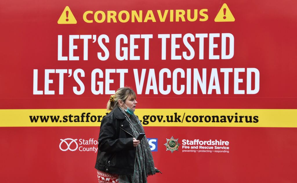 Mujer camina ante cartel que promueve la vacunación anticovid en Inglaterra