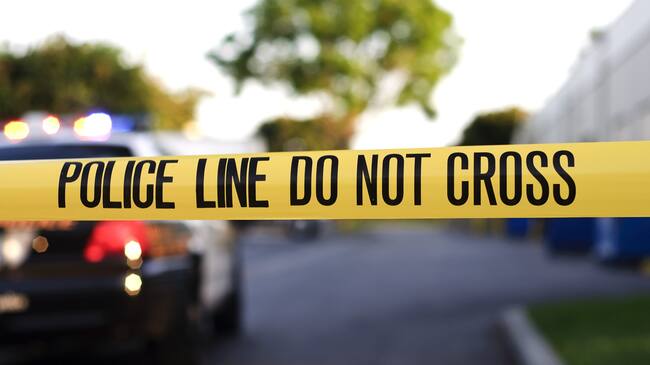 A blurred police car in the background behind yellow crime scene tape.