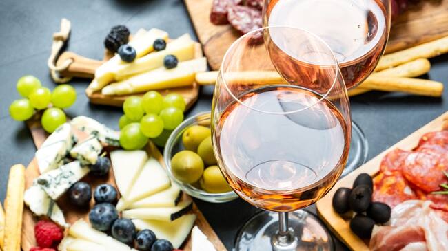 Aperitif two glasses of French rose wine with cheese and salami, olives and grapes