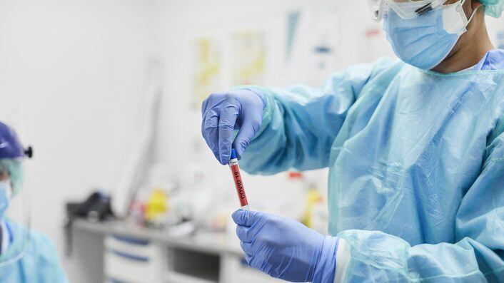 Midsection of male doctor holding medical sample test tube at examination room. Medical expertise doing research on COVID-19 at hospital. He is wearing protective workwear.
