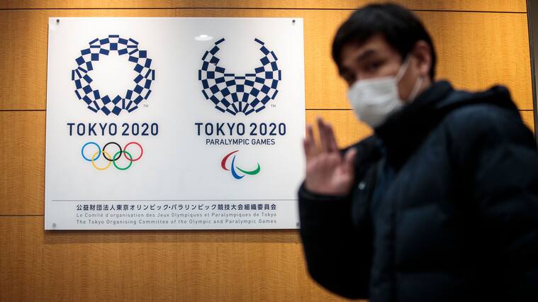 A reporter gestures as he walks past the logos of Tokyo 2020 Olympic and Paralympic Games after a press conference at the Tokyo 2020 headquarters in Tokyo on March 30, 2020. - The postponed Tokyo 2020 Olympics will open on July 23, 2021, organisers said on March 30, announcing the new date after the Games were delayed because of the coronavirus pandemic. The decision comes less than a week after organisers were forced to delay the Games under heavy pressure from athletes and sports federations as the global outbreak took hold. (Photo by Behrouz MEHRI / AFP) (Photo by BEHROUZ MEHRI/AFP via Getty Images)