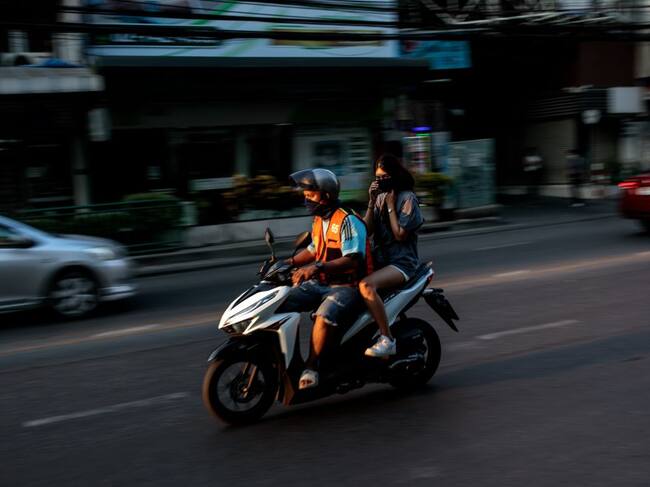 A woman rides on the back of a motorbike taxi in Bangkok on December 18, 2020. (Photo by Jack TAYLOR / AFP) (Photo by JACK TAYLOR/AFP via Getty Images)