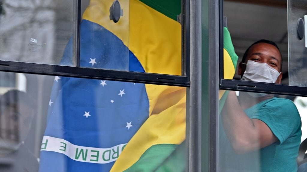 A Brazilian citizen shows a national flag from a bus taking him and others to the Jorge Chavez international airport in Callao, outside the Brazilian consulate in Lima, on March 20, 2020, due to coronavirus lockdown. - Some 400 Brazilian citizens are being repatriated after remaining stranded due to the closure of borders and the mandatory quarantine decreed by the Peruvian government as a preventive measure against the coronavirus pandemic. 263 people have tested positive and four have died in Peru so far from the new coronavirus, COVID-19. (Photo by Cris BOURONCLE / AFP) (Photo by CRIS BOURONCLE/AFP via Getty Images)