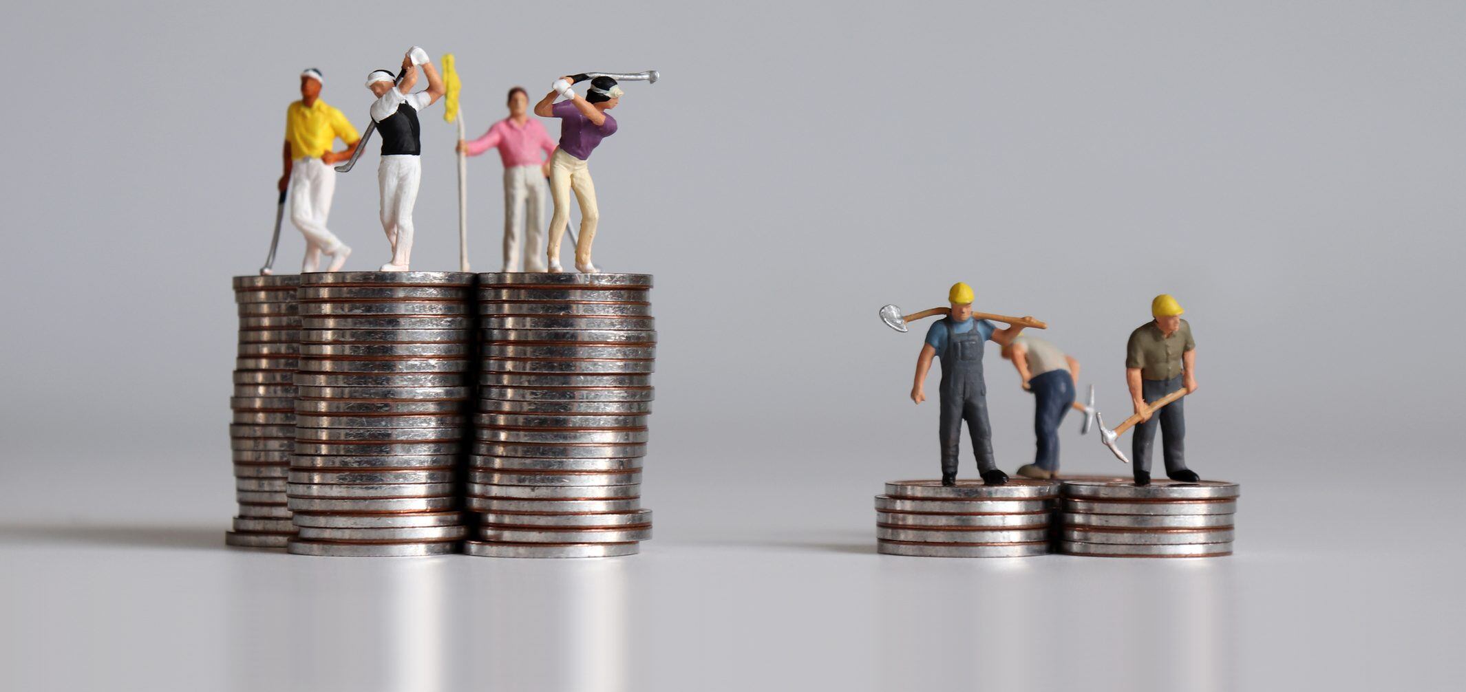 Concept of the gap between rich and poor. Miniature people standing on a pile of coins.