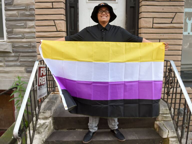 Kathiria "Ezra" Zorrilla poses holding a non-binary flag