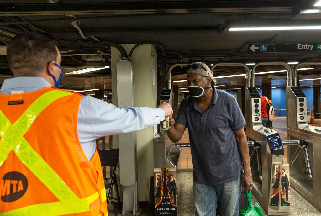 Trabajador entrega desinfectante a pasajero del Metro de Nueva York