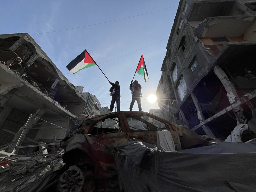 Dos niños en la Franja de Gaza ondean la bandera de Palestina sobre la destrucción que dejaron los ataques de Israel