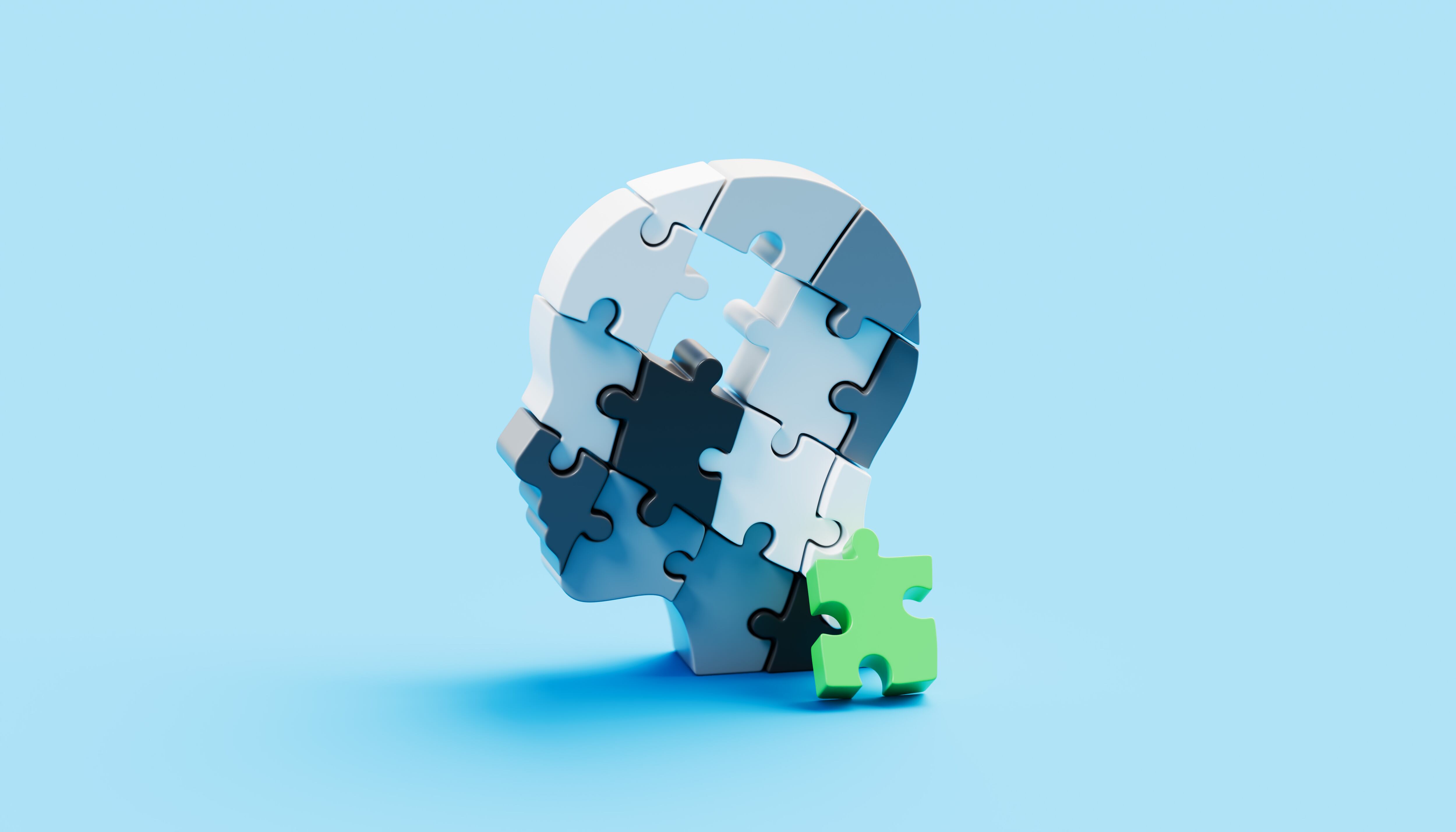 A conceptual head shape made of interlocking puzzle pieces features a single green piece missing from the brain area, shown resting against the side of the puzzle. This symbolic composition represents the fragility and complexity of the human mind, highlighting themes of memory, cognition, and mental health. The missing piece suggests gaps, challenges, or struggles within mental processes, while its presence nearby conveys the potential for healing, recovery, and restoration. The image serves as a metaphor for resilience, problem-solving, and the ongoing journey toward wholeness and balance.