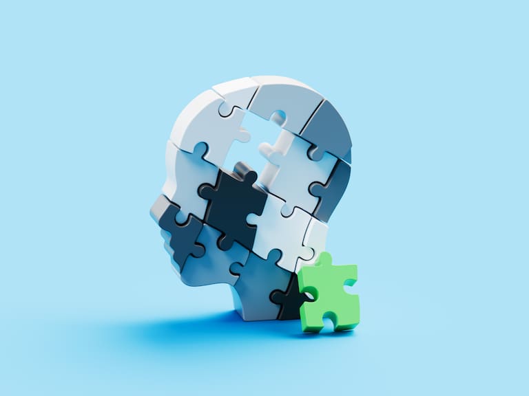 A conceptual head shape made of interlocking puzzle pieces features a single green piece missing from the brain area, shown resting against the side of the puzzle. This symbolic composition represents the fragility and complexity of the human mind, highlighting themes of memory, cognition, and mental health. The missing piece suggests gaps, challenges, or struggles within mental processes, while its presence nearby conveys the potential for healing, recovery, and restoration. The image serves as a metaphor for resilience, problem-solving, and the ongoing journey toward wholeness and balance.