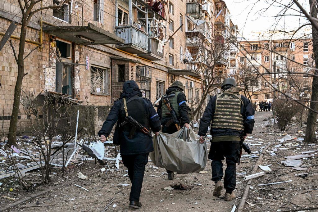 TOPSHOT - Ukrainian policemen carry a body away from a five-storey residential building that partially collapsed after a shelling in Kyiv on March 18, 2022, as Russian troops try to encircle the Ukrainian capital as part of their slow-moving offensive. - Authorities in Kyiv said one person was killed early today when a downed Russian rocket struck a residential building in the capital's northern suburbs. They said a school and playground were also hit. (Photo by Sergei SUPINSKY / AFP) (Photo by SERGEI SUPINSKY/AFP via Getty Images)