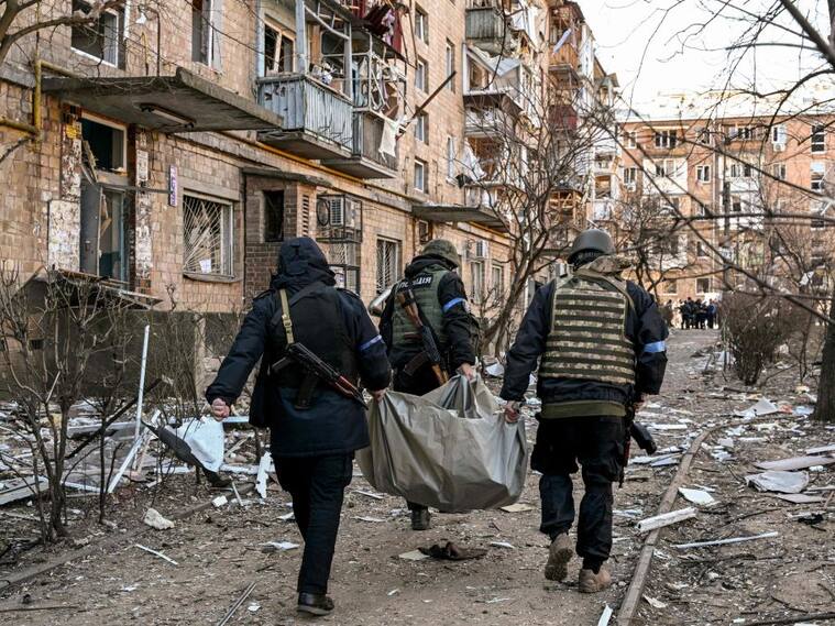 TOPSHOT - Ukrainian policemen carry a body away from a five-storey residential building that partially collapsed after a shelling in Kyiv on March 18, 2022, as Russian troops try to encircle the Ukrainian capital as part of their slow-moving offensive. - Authorities in Kyiv said one person was killed early today when a downed Russian rocket struck a residential building in the capital's northern suburbs. They said a school and playground were also hit. (Photo by Sergei SUPINSKY / AFP) (Photo by SERGEI SUPINSKY/AFP via Getty Images)