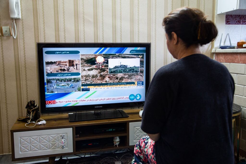 Una mujer mira la televisión en Teherán, luego que Irán fuera atacado con drones en diferentes zonas de ese país.