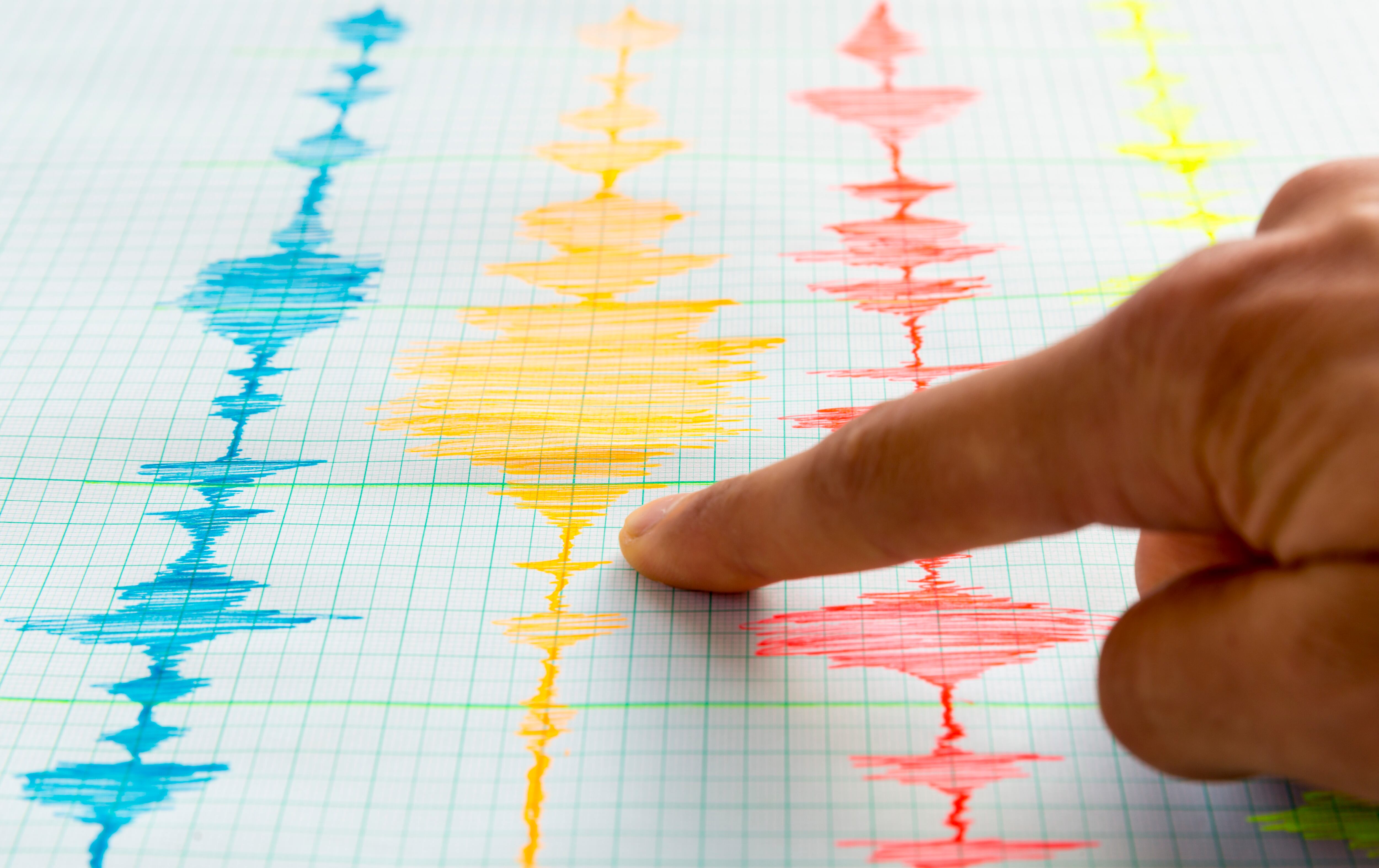 Seismological device for measuring earthquakes. Seismological activity live on the sheet of measuring paper. Earthquake wave on graph paper. Human hand showing earthquake.